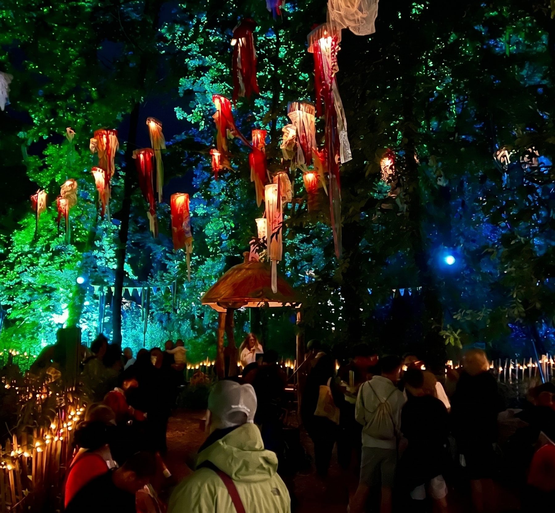 A night forest at a festival, glowing lanterns hanging from the trees over a crowd walking in